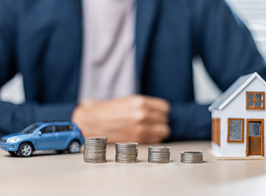 coins-stacked-in-front-of-house-model-and-toy-car-symbolize-financial-planning